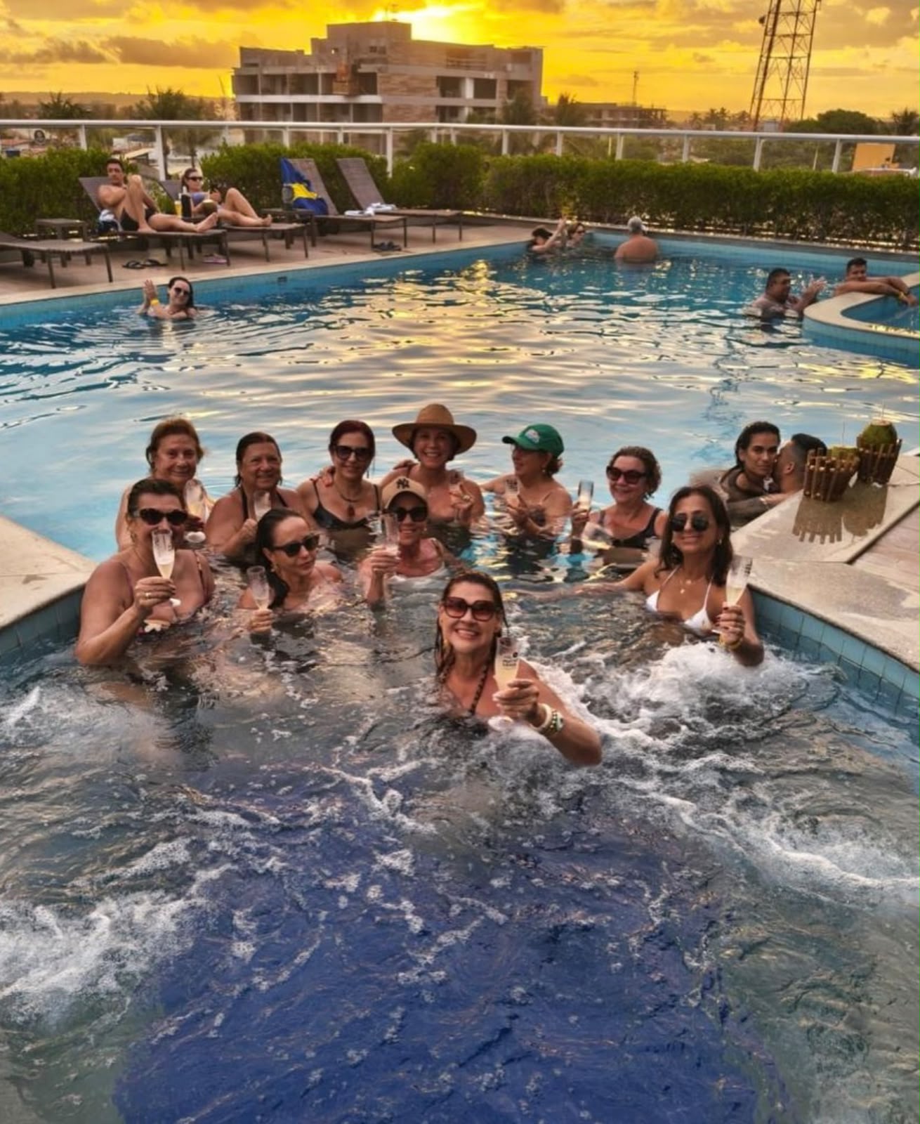 Grupo brindando na piscina ao pôr do sol